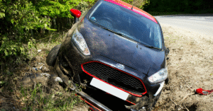 Black Ford car with red accents stuck in a ditch off a rural road.